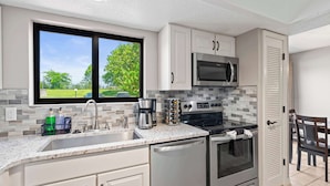 A modern kitchen with a large window, stainless steel appliances, and a tiled backsplash. - Lake Ozark Oasis Central Location & Pool Access (Lake Ozark)