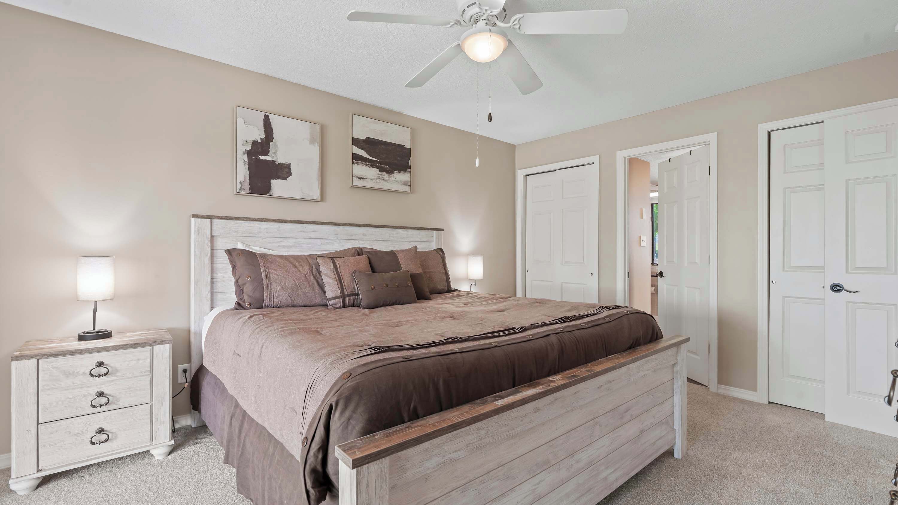 A bedroom with a bed, bedside tables, a ceiling fan, and two doors.