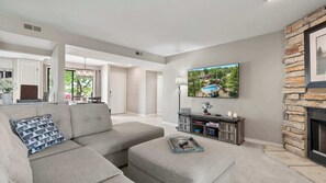 A modern living room with a sectional sofa, a fireplace, a mounted TV, and a dining area with natural light. - Lake Ozark Oasis Central Location & Pool Access (Lake Ozark)