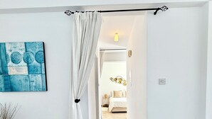 Un corridoio che conduce a una camera da letto con un letto, una tenda bianca, un dipinto astratto blu e un tappeto tessuto.
