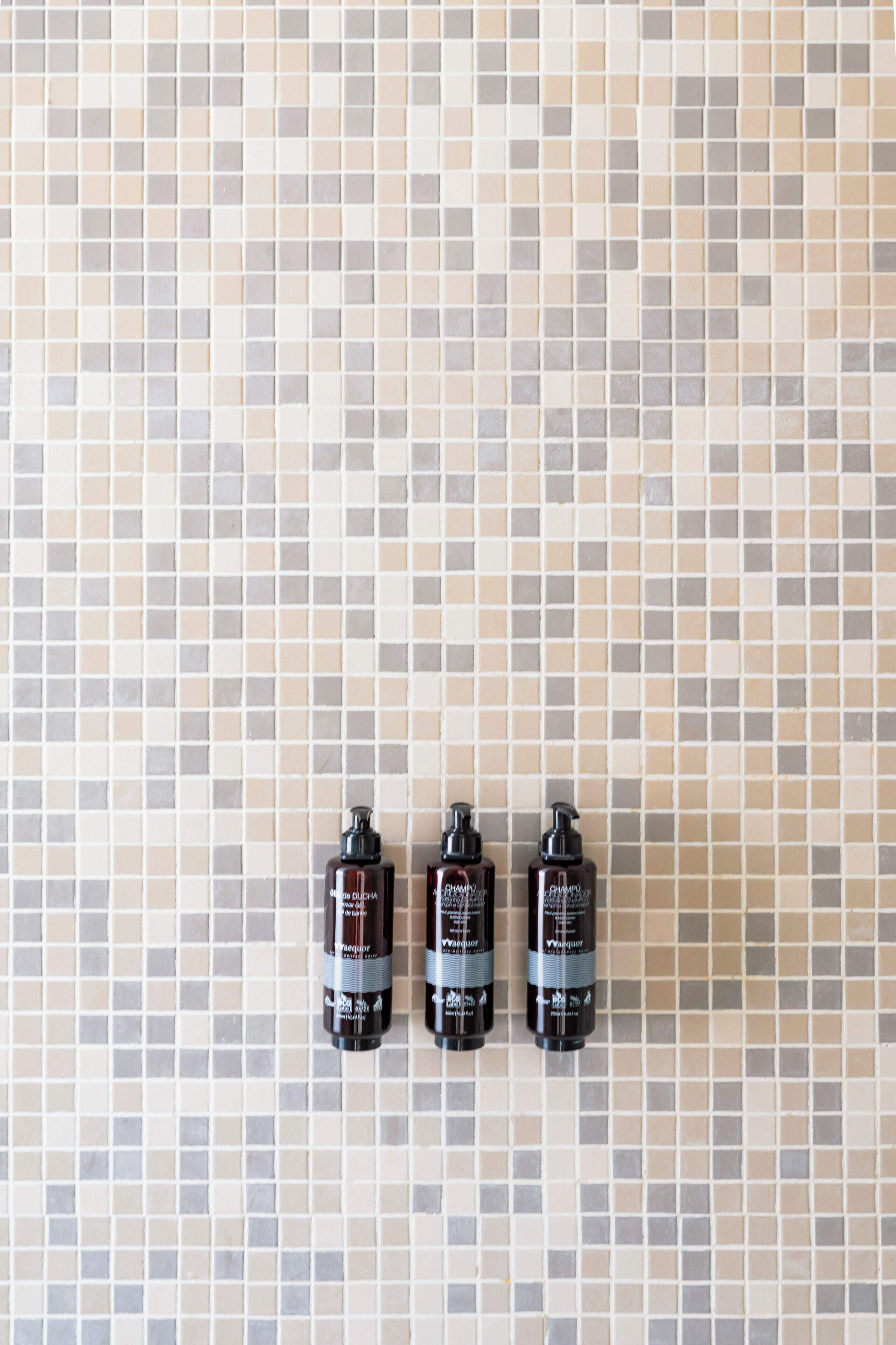 Three bottles of shampoo on a tiled wall.