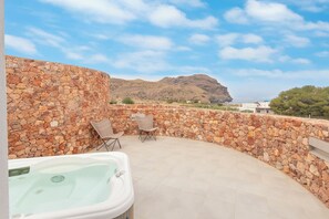 Un espacio al aire libre con paredes de piedra, una bañera de hidromasaje, sillas y vistas a una montaña.
