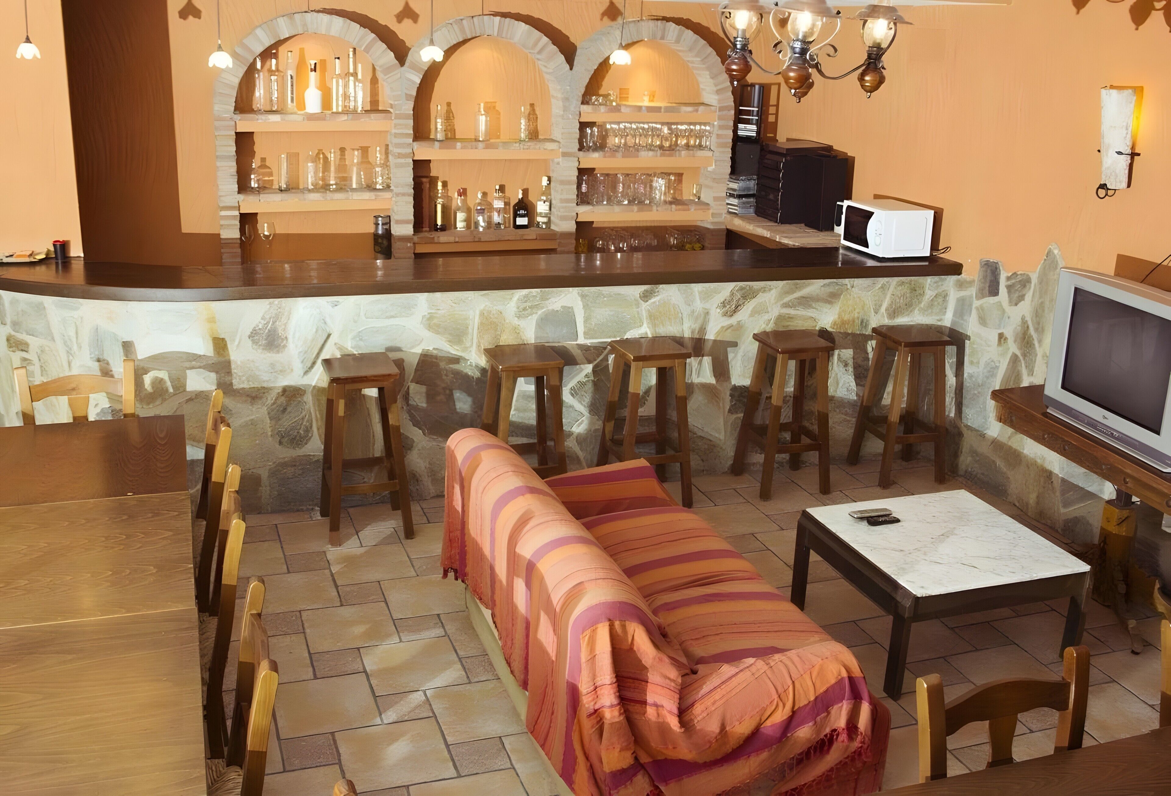 Zona de bar con paredes de piedra, taburetes de madera y una barra con botellas y vasos.