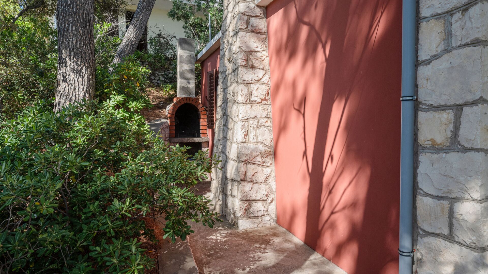 Um caminho estreito leva a um edifício de pedra com forno de tijolos, em meio à vegetação.