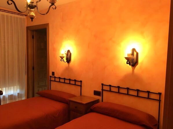A hotel room with two beds, a nightstand, a wall-mounted light fixture, and a door.