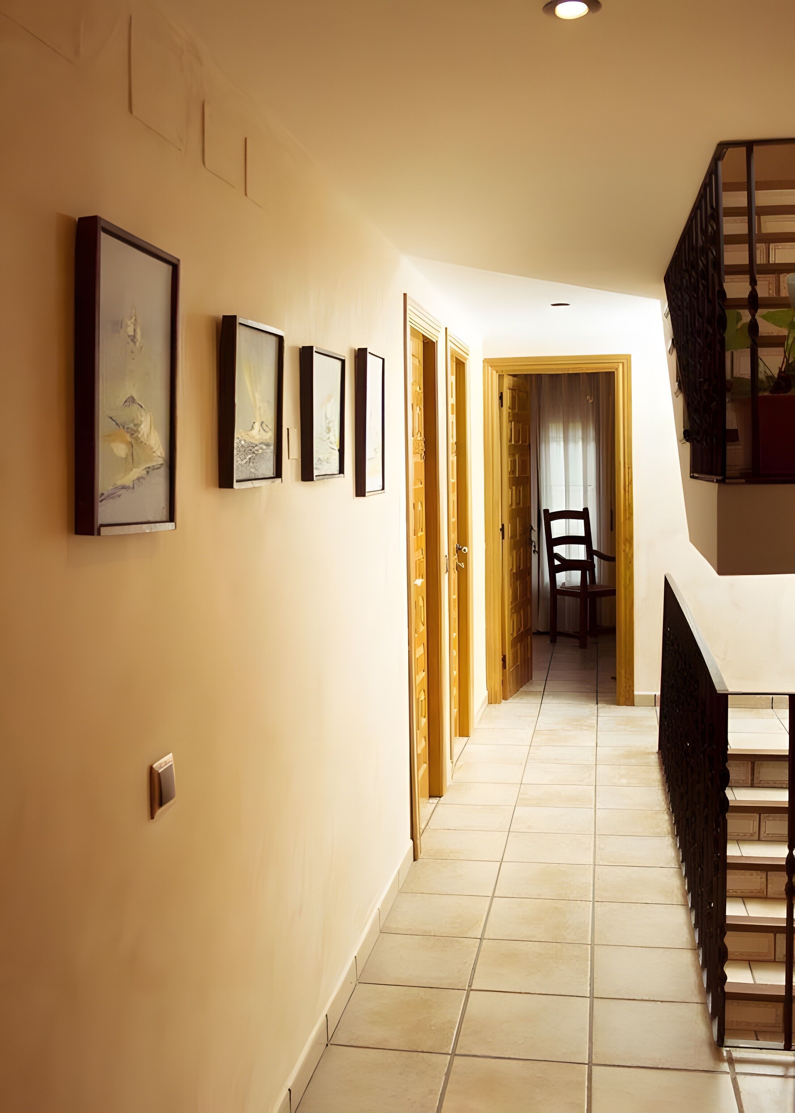 A hallway with framed artwork on the walls, wooden doors, and a staircase with a black railing.