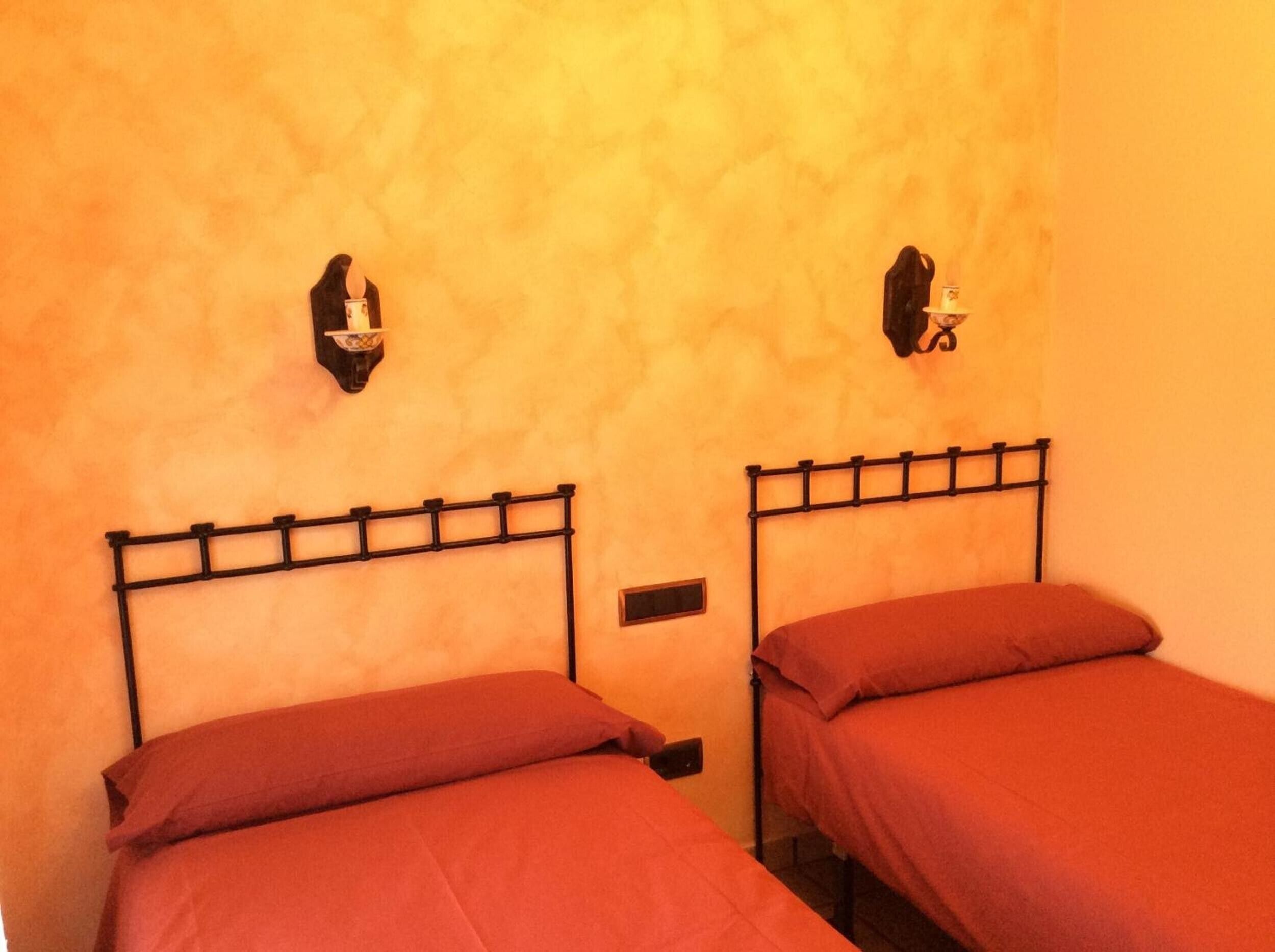 Deux lits avec des cadres en métal, un radiateur fixé au mur et un luminaire fixé au mur.