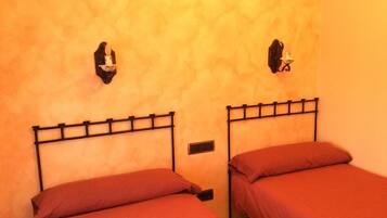 Deux lits avec des cadres en métal, un radiateur fixé au mur et un luminaire fixé au mur.