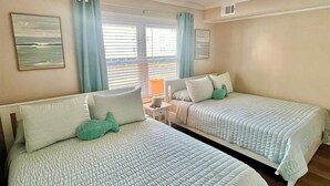 A bedroom with two beds, a ceiling fan, a window with blinds, and a small table with a lamp. - New for 2026! Ocean Block and Fully Renovated! Comfortably sleeps 6, FREE Linens (Ocean City)