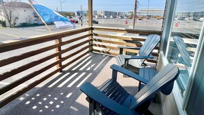 A balcony with wooden railings, two Adirondack chairs, and a view of a street with vehicles and buildings. - New for 2026! Ocean Block and Fully Renovated! Comfortably sleeps 6, FREE Linens (Ocean City)