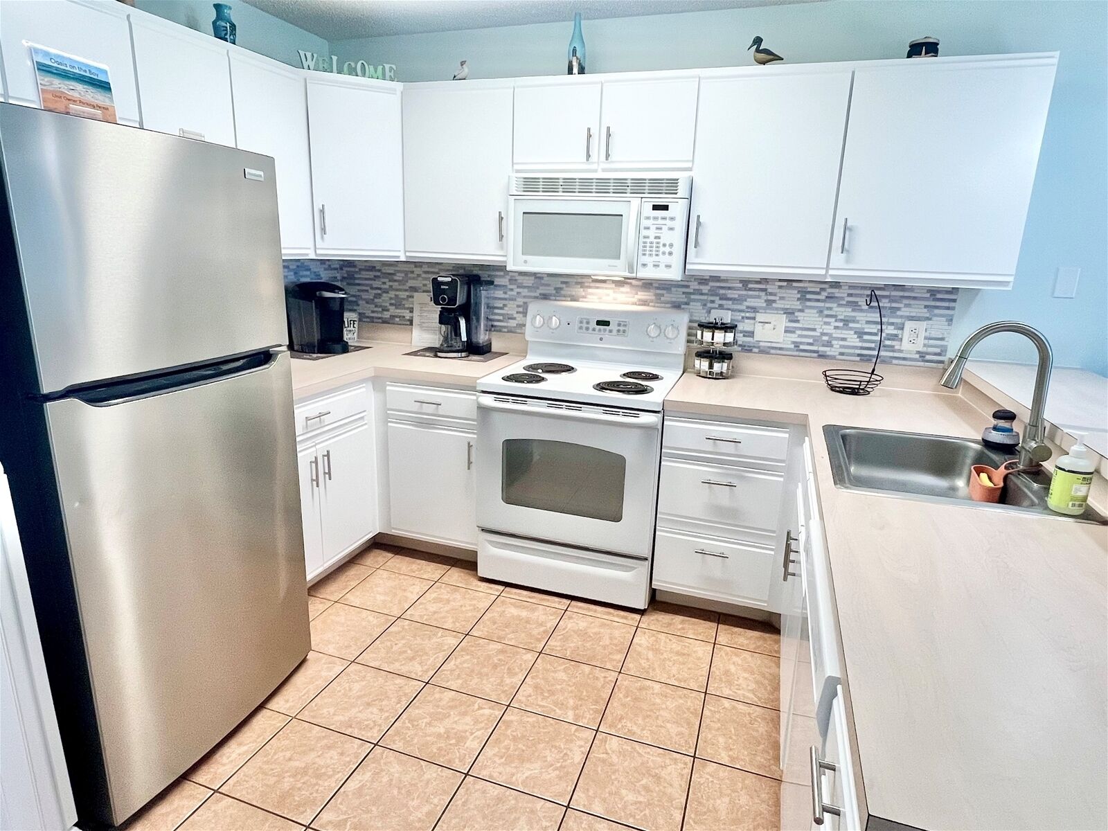 A compact kitchen with white cabinets, a stainless steel refrigerator, a microwave, a stove, and a sink.