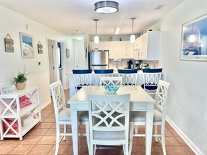 A modern kitchen with white cabinets, a stainless steel range hood, and blue chairs around a white table. - New 2026! Bayfront, FREE Linens & Towels, Outdoor Pool, Walk to Fager's Island (Ocean City)
