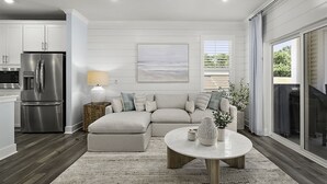 En moderne stue med en modulsofa, et rundt sofabord og et køkken med et rustfrit stål køleskab.