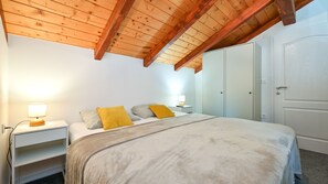 A bedroom with a wooden ceiling, a bed with a grey blanket, two bedside lamps, and a wardrobe.