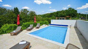 A rooftop swimming pool with lounge chairs and umbrellas, surrounded by greenery.
