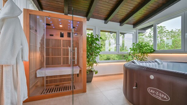 Et saunaområde med et glasafsnit, et massagebord og et spabad mærket 'LAY-Z-SPA. MALDIVES'.