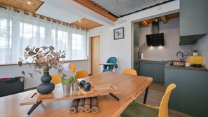 A modern kitchen with a TV, a dining area with a wooden table, chairs, and a vase with flowers.
