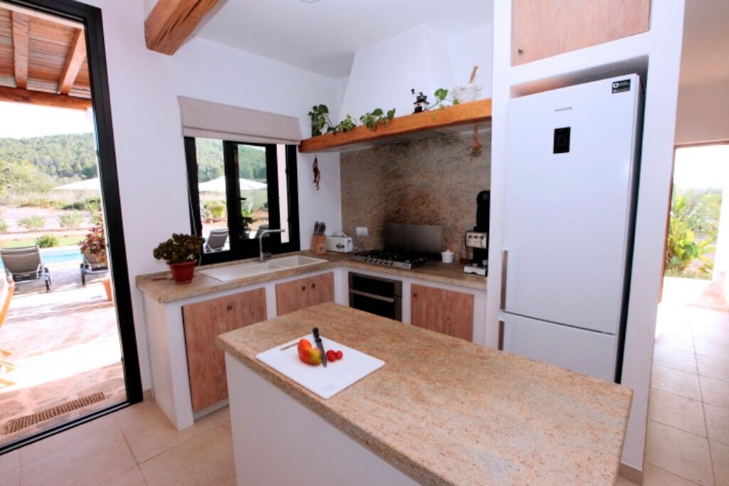 A kitchen with a granite countertop, a refrigerator, and a window overlooking a garden.