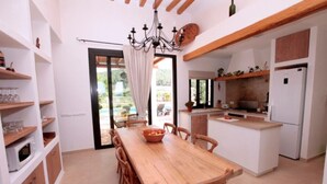 A modern kitchen with a wooden dining table, white cabinets, and a built-in island. - Charming villa in the middle of nature (Sant Miquel de Balansat)