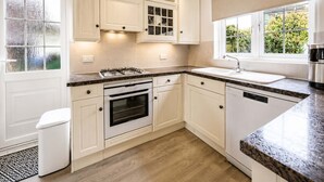 Cocina moderna con gabinetes blancos, horno integrado, estufa de acero inoxidable y ventana con vista a vegetación.