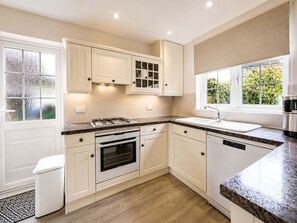 Cocina moderna con gabinetes blancos, horno integrado, estufa de acero inoxidable y ventana con vista a vegetación.
