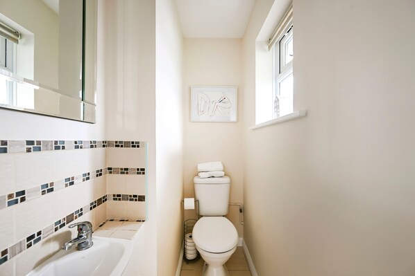 Een badkamer met een wit toilet, een wastafel met een chromen kraan, een betegelde spatwand en een kunstwerk in een lijst aan de muur.