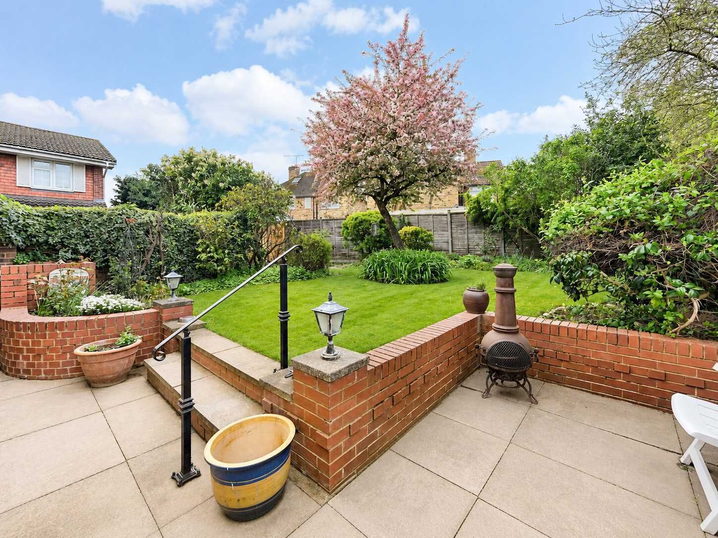 A patio area with a brick wall, a barbecue grill, a large pot, and a white chair.