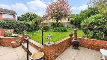 A patio area with a brick wall, a barbecue grill, a large pot, and a white chair.