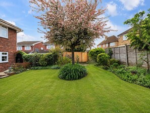 Un jardín residencial con un césped cuidado, distintos arbustos y un árbol en flor.