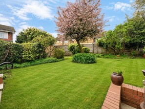 A well-maintained garden with a lawn, a variety of shrubs, and a flowering tree.