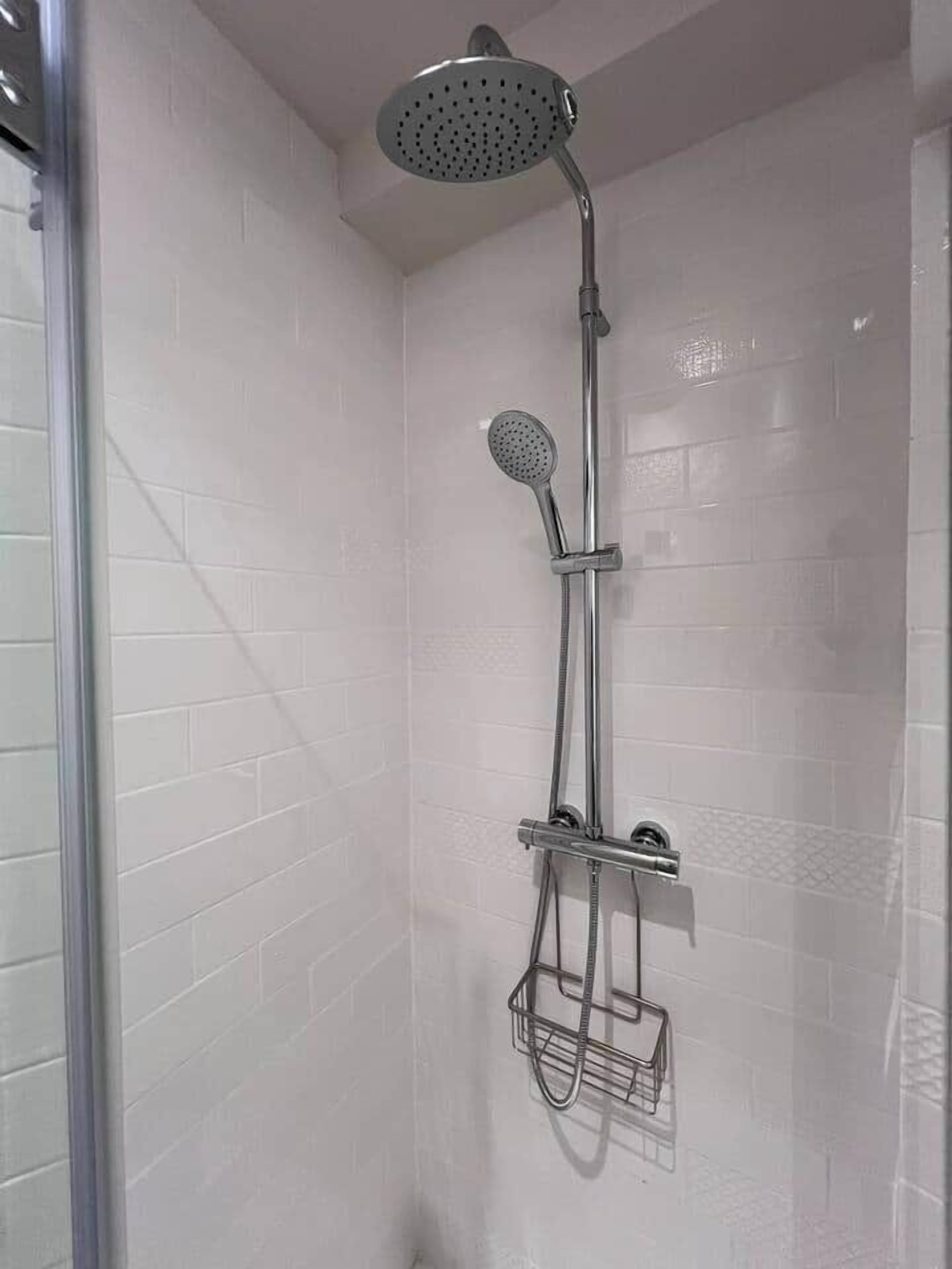 A shower with a handheld showerhead and a fixed showerhead, mounted on a wall with white tiles.