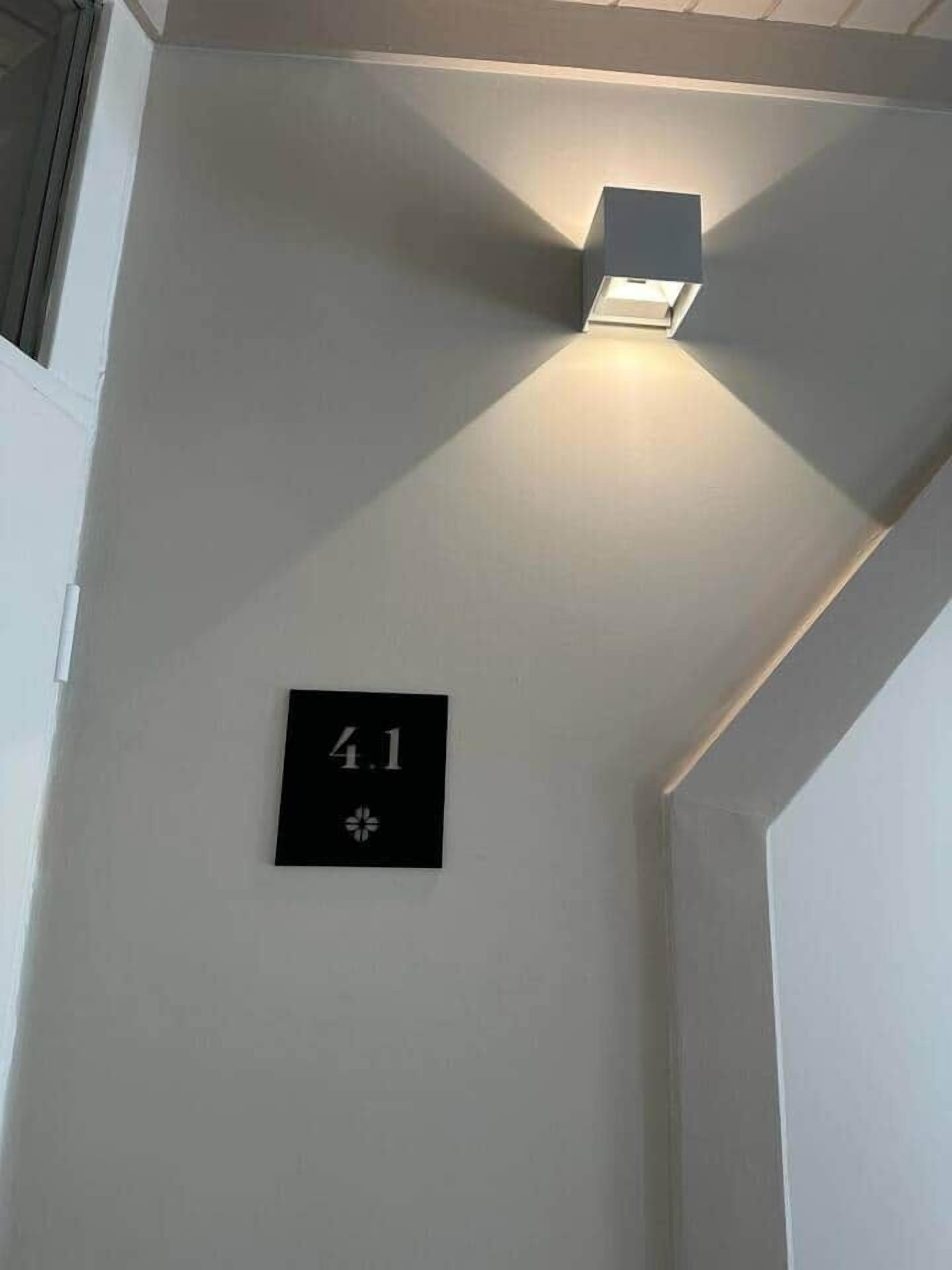 Een bordje aan de muur met het nummer '4.1' en een symbool, en een lamp aan het plafond.