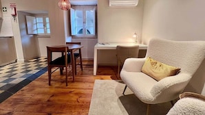 A room with a wooden floor, a white sofa, a dining table with chairs, a desk, and a window with curtains. - CorpusChristi 35-12 (Coimbra)