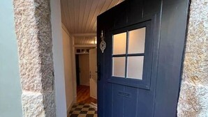 A hallway with a checkered floor, a dark door with a window, and stone walls. - CorpusChristi 35-12 (Coimbra)