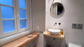A bathroom with a window, a sink, a mirror, a toilet, and a checkered floor.