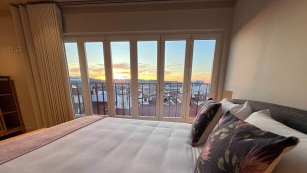 Quarto de hotel com uma cama grande, vista para a cidade e uma janela com cortinas.