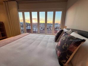 A hotel room with a large bed, a view of the cityscape, and a window with curtains. - CorpusChristi 35-31 (Coimbra)