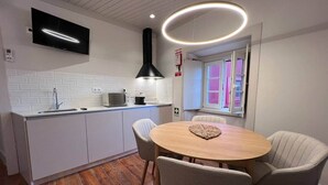 Cozinha moderna com armários brancos, uma mesa de jantar de madeira e uma TV instalada acima do balcão.
