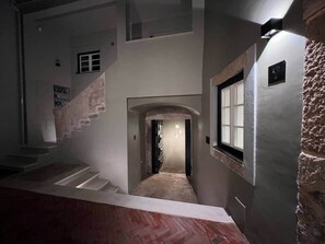 Un couloir avec un escalier, une porte dotée d’une fenêtre et un mur en pierre.