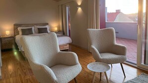 Una camera d'albergo con un letto, due poltrone, un tavolino, un comodino e un'ampia finestra con vista.
