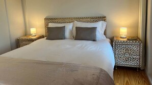 Un letto rifatto con cura, una testiera decorata, due comodini con lampade e un pavimento in legno.
