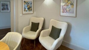 Ein Zimmer mit zwei weißen Sesseln, einem Holztisch und zwei gerahmten Kunstwerken an der Wand.
