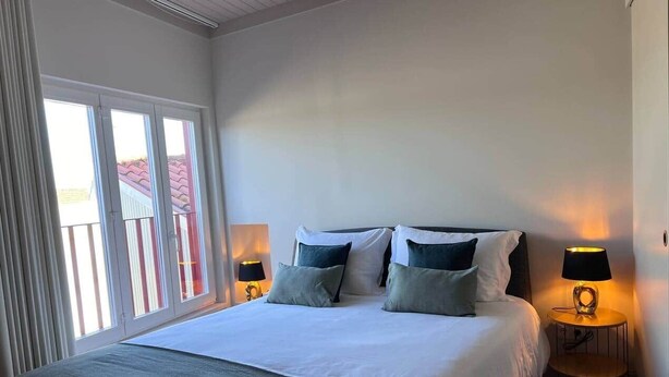 Ein Schlafzimmer mit einem großen Bett, zwei Nachttischlampen und Blick durch ein Fenster.