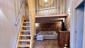 Una habitación estilo loft con escalera de madera, pared de piedra, sofá y un jarrón decorativo.