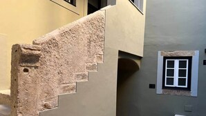 Una escalera con fachada de piedra, un ventanal con marco blanco y una pared lisa.