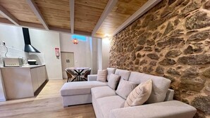 Una sala de estar con pared de piedra, techo de madera, un sofá y una zona de cocina.