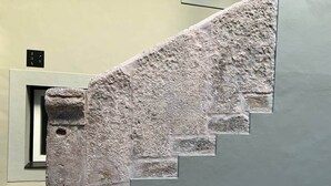 Un escalier en pierre à la surface texturée, menant à une porte dotée d’une petite fenêtre.