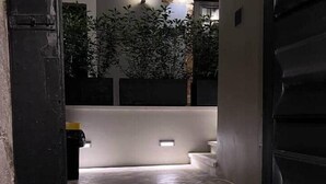 Un couloir intérieur doté d’un sol en pierre, une porte noire sur la gauche et un mur blanc avec un luminaire.