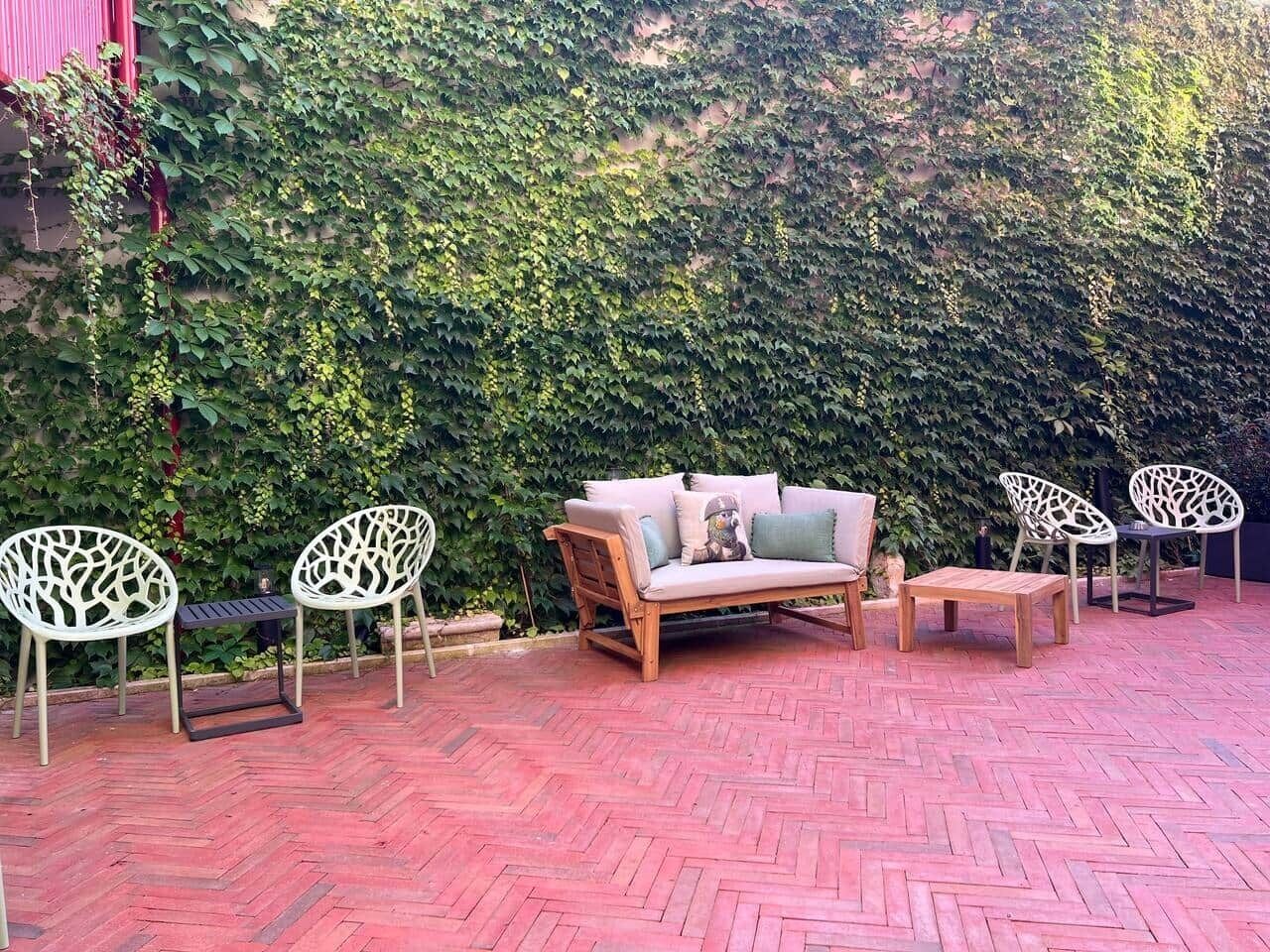 An outdoor seating area with a wooden sofa, two white chairs, and a small table.