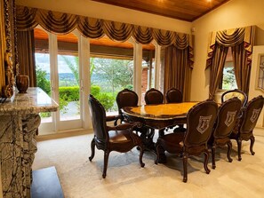 Un comedor con una gran mesa de madera y seis sillas, ventanas amplias con cortinas y una chimenea de piedra.